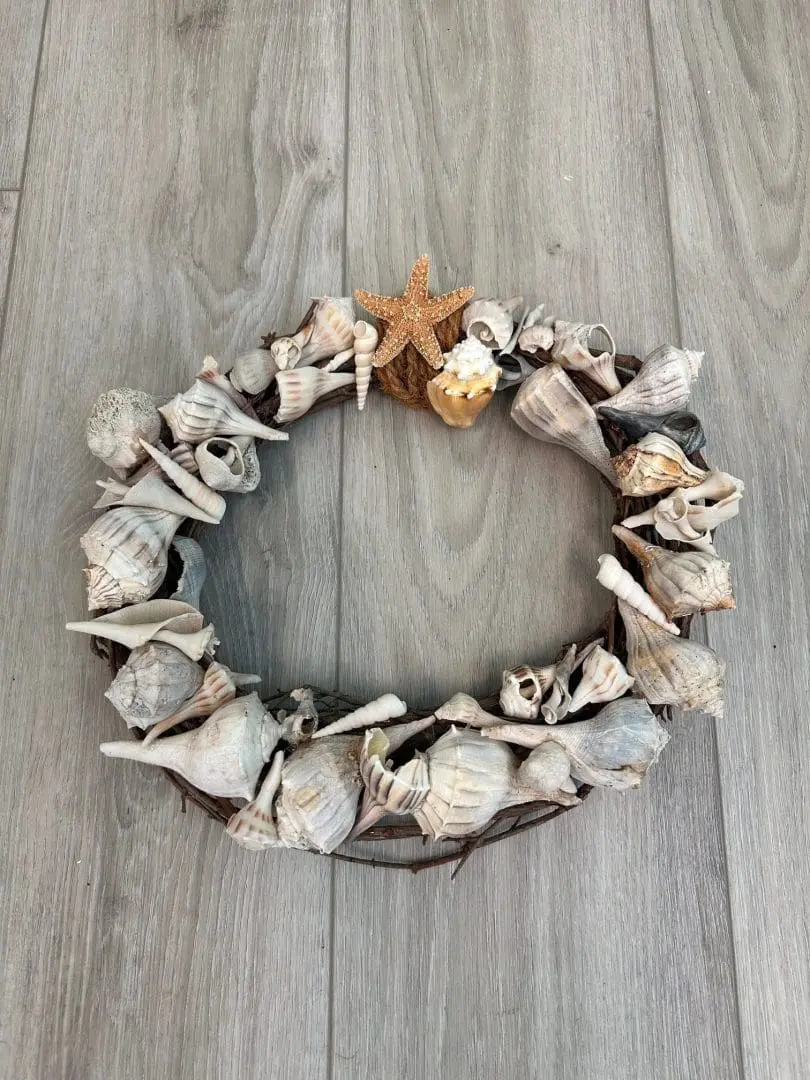 Shell wreath adorned with various seashells and a starfish, placed on a light wooden surface, representing the arts and crafts event at Gulf Waters Beach Front RV Resort.