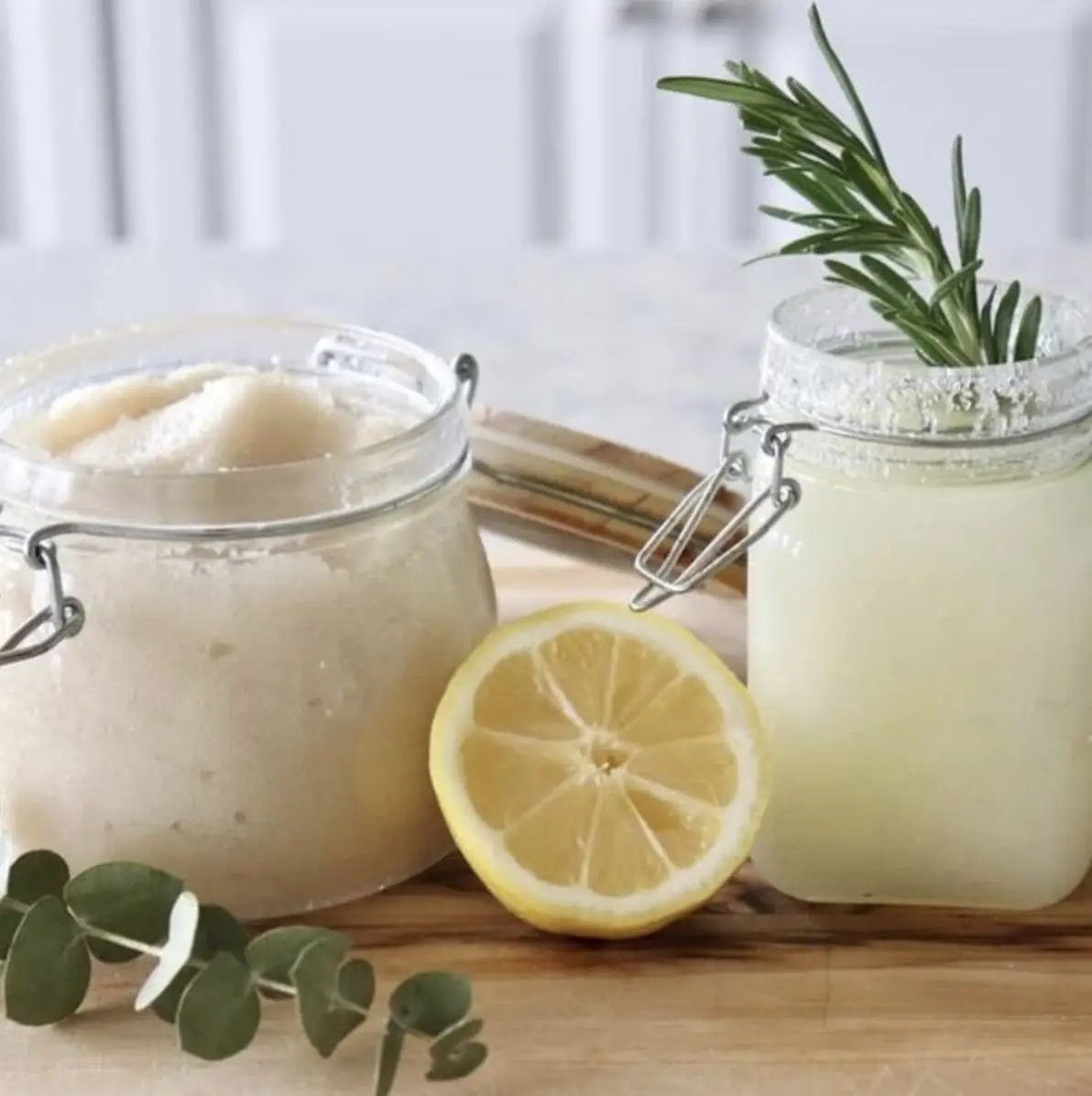 Glass jars of homemade salt scrubs with a lemon slice and eucalyptus leaves, showcasing ingredients for DIY skin care at Gulf Waters event.