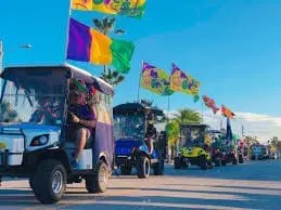 Golf carts decorated with Mardi Gras flags in a parade at Gulf Waters Beach Front RV Resort, showcasing festive colors and community celebration.