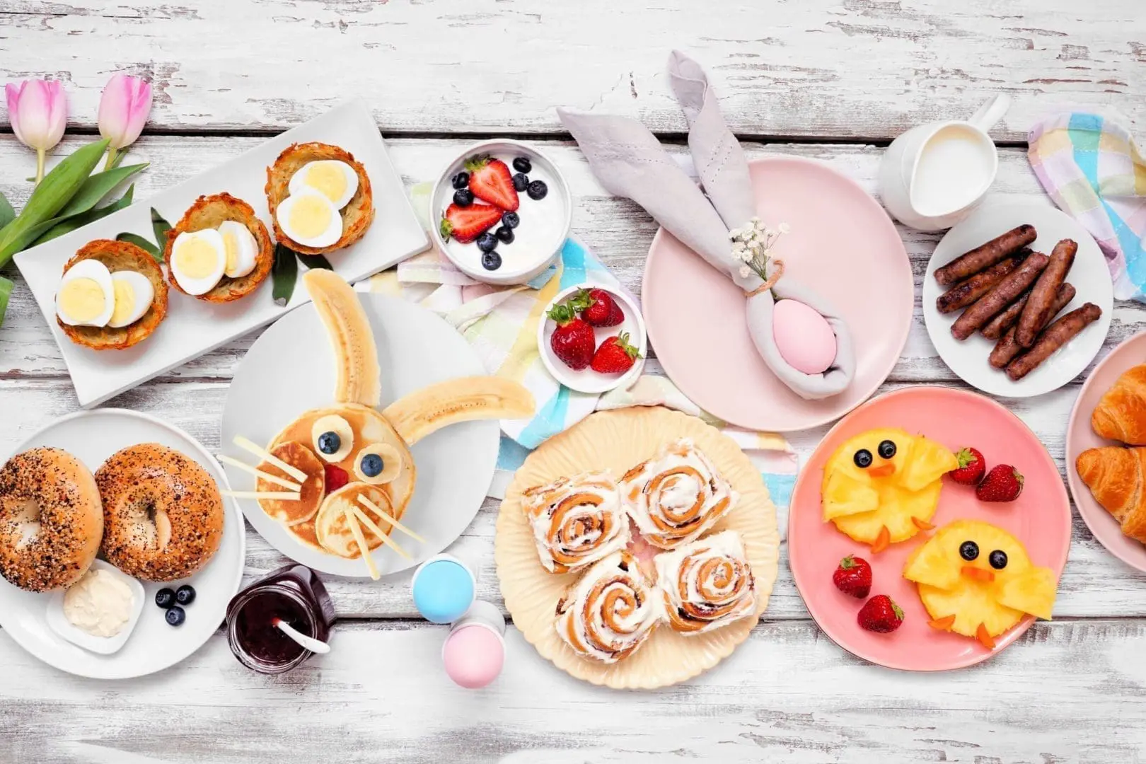 Easter brunch spread featuring decorative food items like bunny-shaped pancakes, egg salad cups, cinnamon rolls, and fruit arrangements, set on a rustic wooden table, ideal for a potluck event at Gulf Waters Beach Front RV Resort.