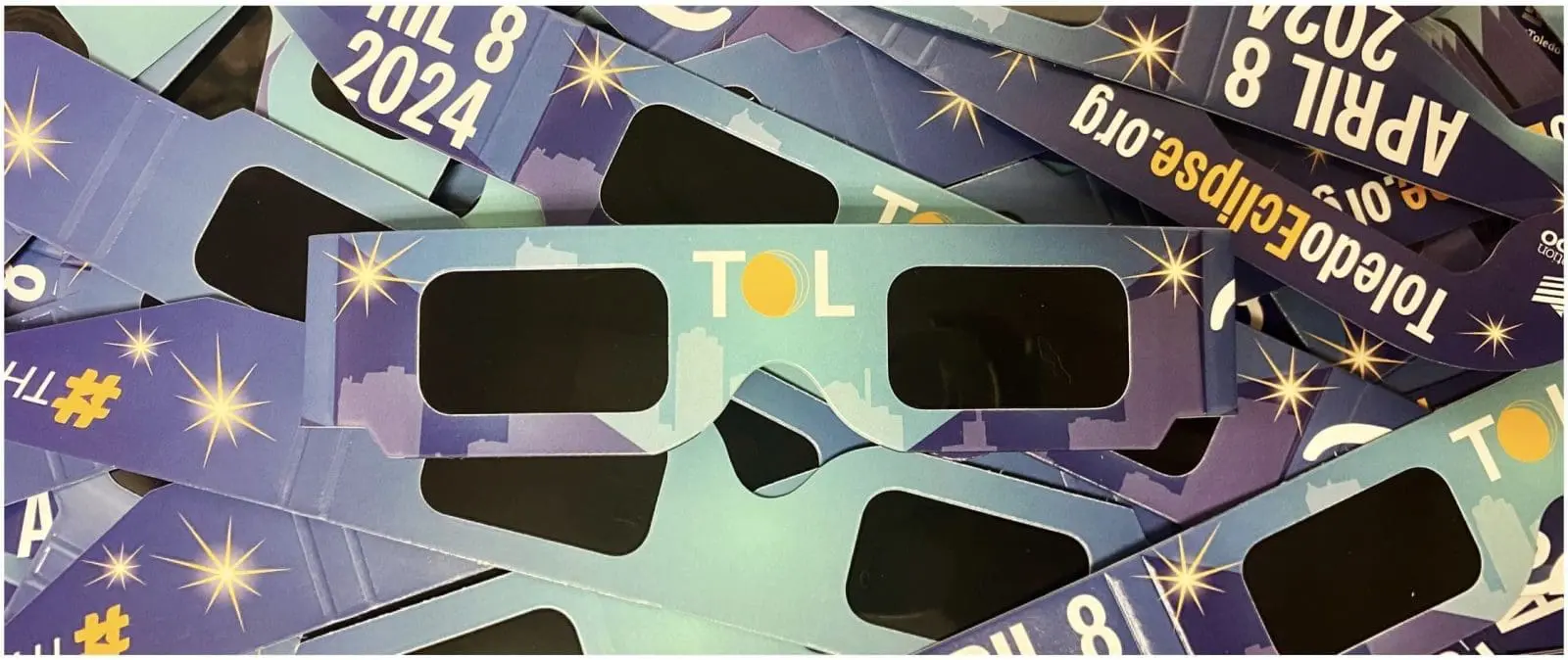 Solar eclipse viewing glasses with "April 8, 2024" and "Toledo Eclipse" branding, stacked together, promoting the Solar Eclipse Beach Party event at Gulf Waters Beach Front RV Resort.