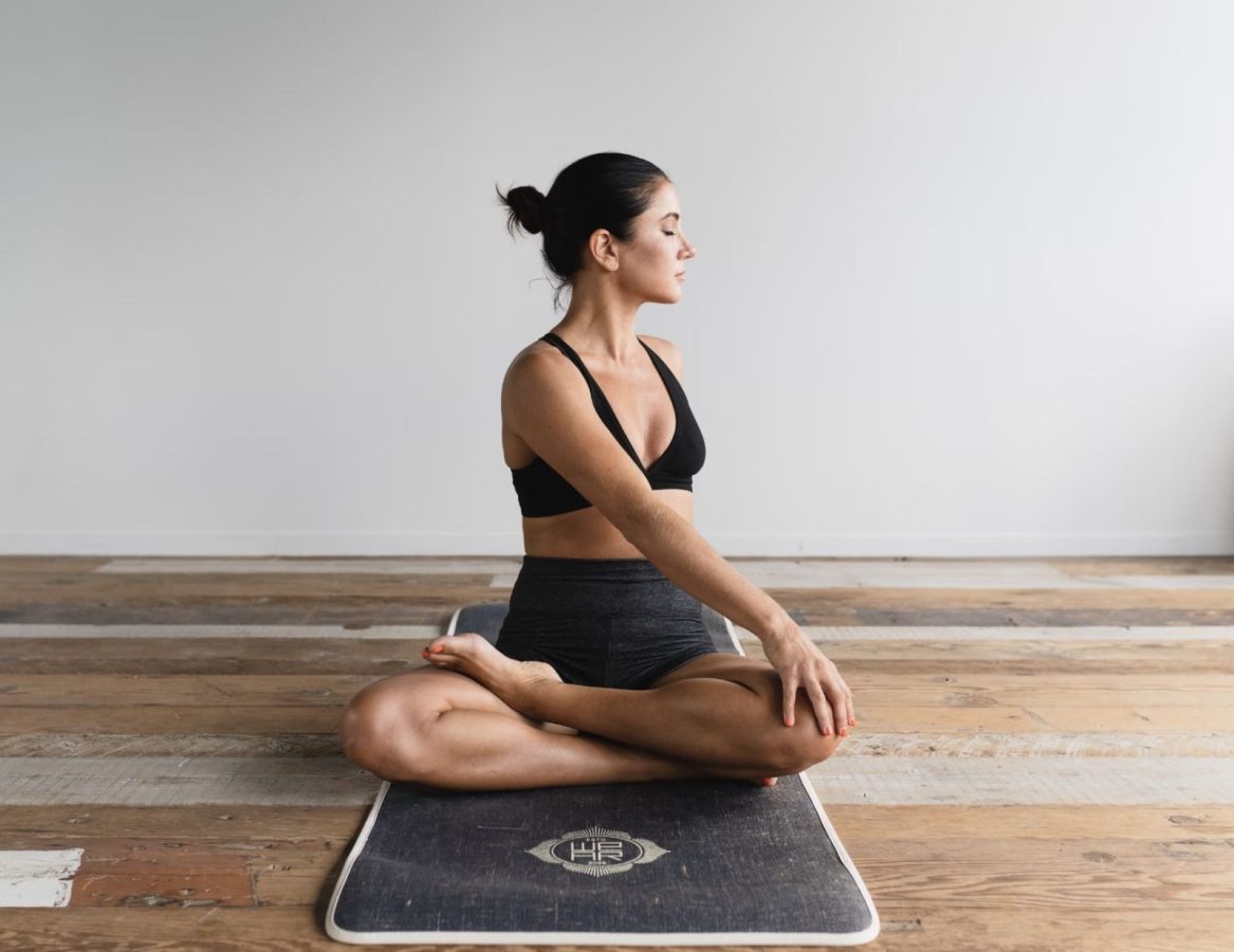 Woman in sports bra and leggings meditating on yoga mat indoors.