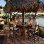 Group of four people enjoying drinks at outdoor table by water at Gulf Waters.