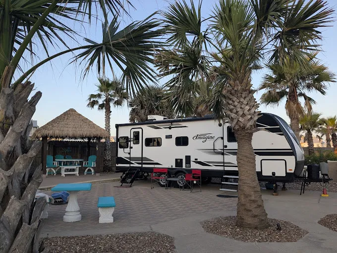 RV parked next to palm trees and a thatched-roof gazebo.