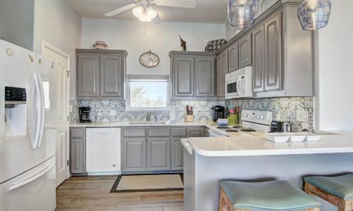 Modern kitchen interior of a beach house rental at Gulf Waters RV Resort, featuring gray cabinetry, stainless steel appliances, and a decorative tile backsplash, designed for comfortable coastal living.