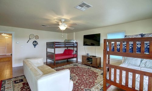Cozy beach house interior featuring a living area with a white sofa, wooden bunk beds, a television, and decorative rug, ideal for family vacations at Gulf Waters Beach Front RV Resort.