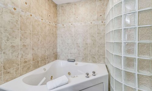 Jacuzzi tub in a modern beach house bathroom with tiled walls and a glass block partition, offering a relaxing retreat for guests at Gulf Waters Beach Front RV Resort.