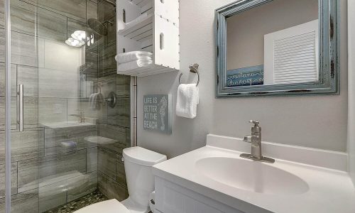 Modern bathroom interior featuring a shower, toilet, and sink, with beach-themed decor and a sign reading "Life is Better at the Beach," reflecting the coastal atmosphere of Gulf Waters Beach Front RV Resort accommodations.