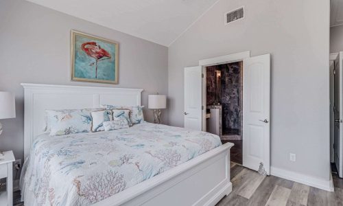Cozy beach house bedroom featuring a king-sized bed with coral-patterned bedding, light gray walls, and modern decor, reflecting the coastal charm of Gulf Waters Beach Front RV Resort.