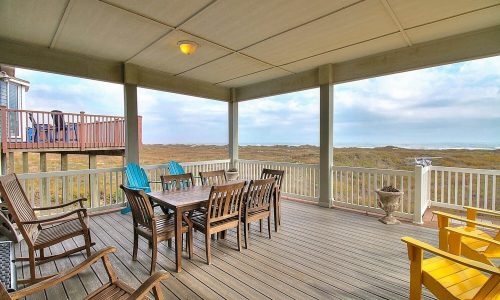 Spacious deck of a beach house at Gulf Waters Beach Front RV Resort, featuring a dining table and colorful chairs, with views of the surrounding landscape and proximity to Mustang Island's sandy shores.