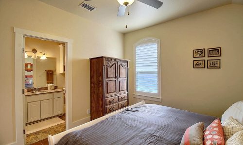 Cozy bedroom in a beach house at Gulf Waters Beach Front RV Resort, featuring a comfortable bed, wooden dresser, and adjoining bathroom, ideal for vacation relaxation.