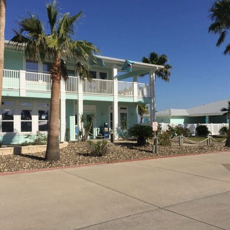 Beachfront RV resort with palm trees and a two-story building under a clear blue sky.