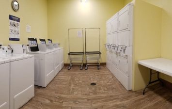 On-site laundry facilities featuring washing machines, drying racks, and folding tables in a bright yellow room, designed for guest convenience after beach activities at Gulf Waters Beach Front RV Resort.