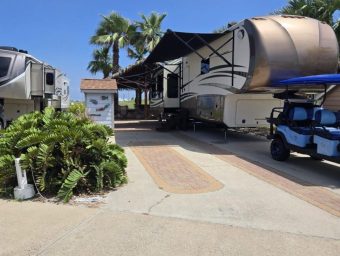 Beachfront RV resort with palm trees, RVs, and a golf cart under a clear blue sky.