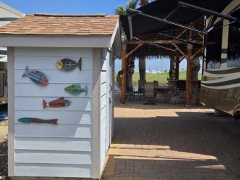 Beachfront RV resort with palm trees, fishing decor, and shaded seating area.
