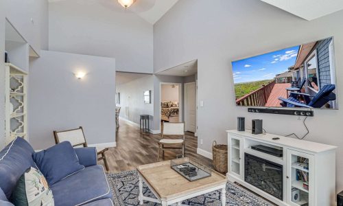 Cozy living room interior of a beach house at Gulf Waters Beach Front RV Resort, featuring modern decor, a large TV displaying a scenic view, and comfortable seating, ideal for family vacations or group retreats near Mustang Island's sandy shores.