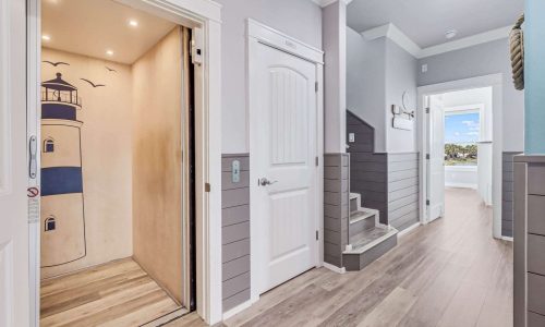 Elevator entrance featuring a lighthouse mural, modern coastal decor, and light wood flooring in a beach house rental at Gulf Waters RV Resort, Mustang Island.