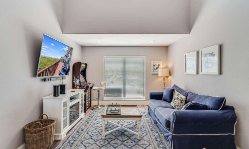 Cozy living room in a beach house at Gulf Waters Beach Front RV Resort, featuring a blue couch, coffee table, modern decor, and a large TV, ideal for relaxing after a day at Mustang Island's sandy shores.