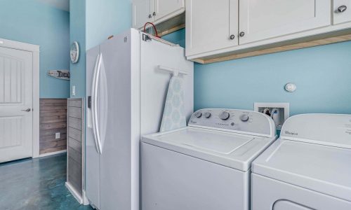 Laundry area featuring a washer and dryer, light blue walls, and modern cabinetry, emphasizing convenience for guests at Gulf Waters Beach Front RV Resort beach house rentals.