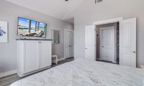 Cozy bedroom interior of a beach house rental at Gulf Waters RV Resort, featuring a white bedspread, flat-screen TV, and coastal decor, emphasizing modern comforts and a relaxing atmosphere for vacationers.