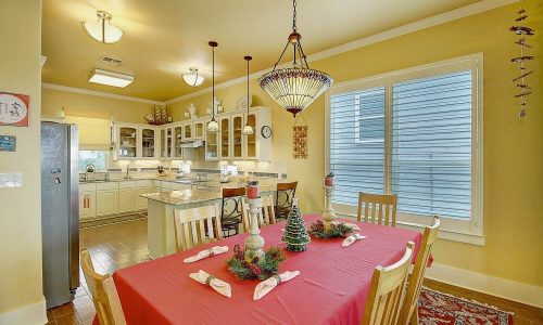 Cozy dining area in a beach house featuring a red table set for a meal, modern kitchen appliances, and bright windows, reflecting the inviting atmosphere of Gulf Waters Beach Front RV Resort accommodations.