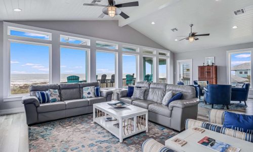 Modern beach house interior with spacious living area, large windows showcasing ocean views, comfortable seating, and coastal decor, reflecting the Gulf Waters RV Resort's rental offerings.