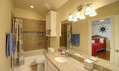 Modern bathroom with granite countertop, shower and tub combination, and blue towels, featuring a doorway leading to a bedroom with a red bedspread, highlighting the stylish accommodations at Gulf Waters Beach Front RV Resort.