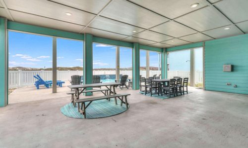 Beach house patio with picnic table and chairs, overlooking Mustang Island's sandy shores, featuring modern coastal decor and bright turquoise accents, ideal for vacation relaxation at Gulf Waters RV Resort.