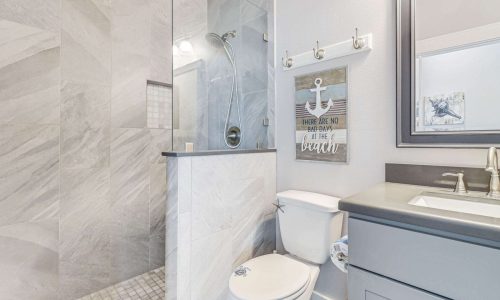 Modern beach house bathroom featuring a walk-in shower with glass enclosure, marble walls, and nautical decor, emphasizing coastal style and comfort for Gulf Waters RV Resort rentals.