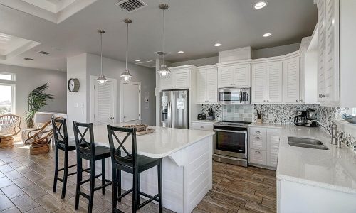 Modern beach house kitchen with white cabinetry, stainless steel appliances, and a large island with bar seating, designed for a comfortable vacation experience at Gulf Waters Beach Front RV Resort.