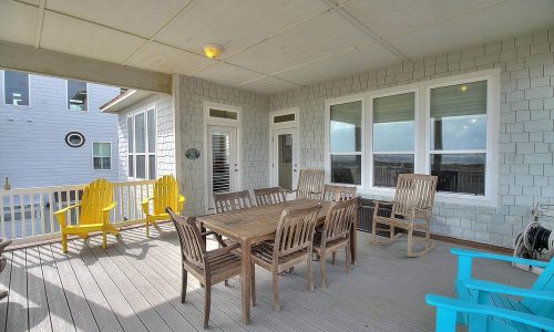 Spacious outdoor patio with wooden dining table and chairs, featuring bright yellow and blue seating, ideal for relaxing and enjoying views at Gulf Waters Beach Front RV Resort beach house.