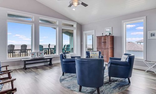Cozy living room in a beach house at Gulf Waters RV Resort, featuring large windows with ocean views, comfortable blue chairs, and modern decor, ideal for a relaxing coastal getaway.