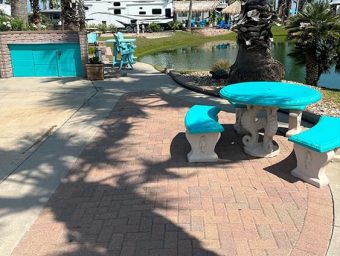 Outdoor seating area with turquoise table and benches beside a pond at Gulf Waters Beach Front RV Resort, showcasing the resort's amenities and inviting atmosphere for lot owners and visitors.