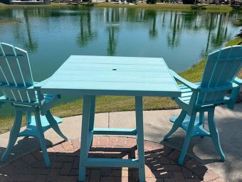 Blue outdoor table and chairs by a serene pond at Gulf Waters Beach Front RV Resort, highlighting relaxation and community amenities.