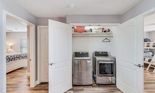 Laundry area with washer and dryer in beach house rental at Gulf Waters Beach Front RV Resort, featuring modern appliances and organized storage, enhancing vacation convenience.
