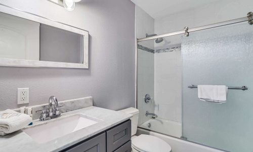 Modern bathroom with a marble countertop, mirror, and glass shower, featuring towels and contemporary fixtures in a beach house at Gulf Waters Beach Front RV Resort.