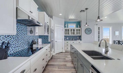 Modern kitchen interior with white cabinetry, blue mosaic backsplash, and stainless steel appliances, showcasing a spacious layout ideal for beach house rentals at Gulf Waters Beach Front RV Resort.