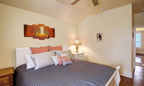 Cozy beach house bedroom with a large bed, decorative pillows, wall art, and bedside lamp, showcasing modern comforts for a relaxing stay at Gulf Waters Beach Front RV Resort.