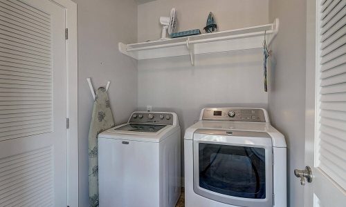 Laundry room featuring modern washing machine and dryer with shelving above, designed for convenience in Gulf Waters Beach Front RV Resort beach house.