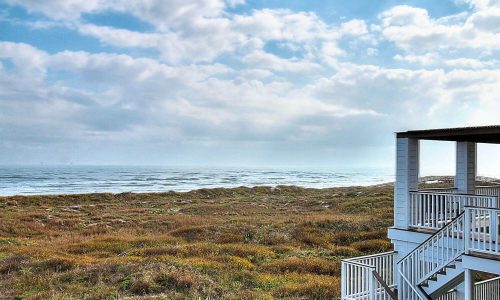 Beach house exterior with steps leading to sandy shores of Mustang Island, overlooking the ocean and coastal landscape, emphasizing a serene beach getaway experience at Gulf Waters Beach Front RV Resort.