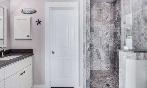 Modern bathroom featuring a sleek design with a shower area, marble tiles, white cabinetry, and coastal decor elements like a starfish and a sign, reflecting the beach house rental experience at Gulf Waters RV Resort.