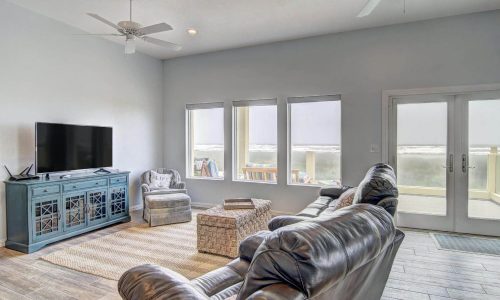 Cozy beach house living room with large windows showcasing ocean views, modern furnishings, and a TV, ideal for relaxing during a stay at Gulf Waters Beach Front RV Resort.