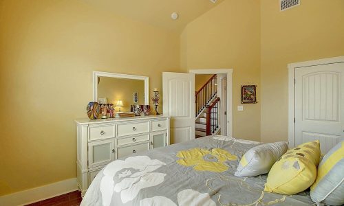 Cozy bedroom in a beach house at Gulf Waters Beach Front RV Resort, featuring a floral-patterned comforter, dresser with decorative items, and a staircase leading to additional rooms.