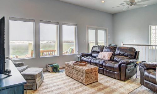 Cozy living room in a beach house rental at Gulf Waters RV Resort, featuring leather seating, large windows with beach views, and modern decor, ideal for family vacations or group getaways.