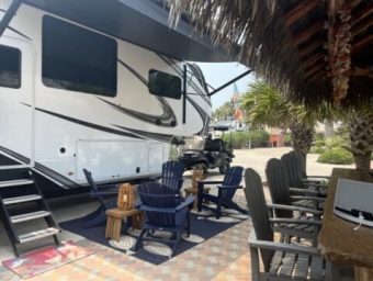 Luxury RV parked at Gulf Waters Beach Front RV Resort with outdoor seating area, palm trees, and a golf cart nearby, showcasing resort amenities and potential vacation lifestyle.