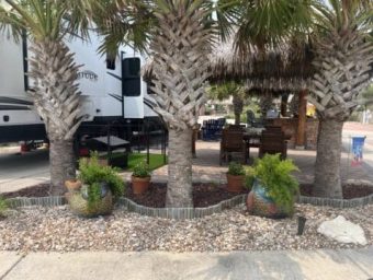 Palm trees and decorative pots in a landscaped RV lot at Gulf Waters Beach Front RV Resort, showcasing outdoor seating area and tropical ambiance.