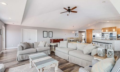 Spacious living room interior of a beach house at Gulf Waters Beach Front RV Resort, featuring modern furnishings, a large sectional sofa, and an open kitchen area, ideal for family vacations and group retreats.