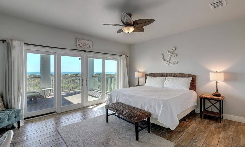 Cozy beach house interior featuring a king-size bed, wooden flooring, and large windows with a view of Mustang Island, ideal for a relaxing getaway at Gulf Waters Beach Front RV Resort.