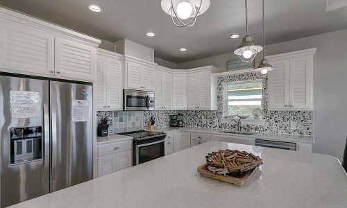 Modern beach house kitchen with white cabinetry, stainless steel appliances, and a spacious island featuring decorative items, showcasing the stylish interior of Gulf Waters Beach Front RV Resort accommodations.