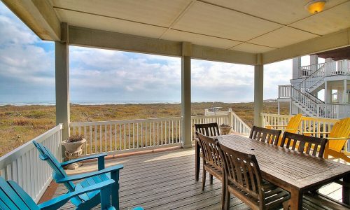 Beach house patio with wooden dining table and chairs, overlooking sandy dunes and beach at Gulf Waters Beach Front RV Resort.